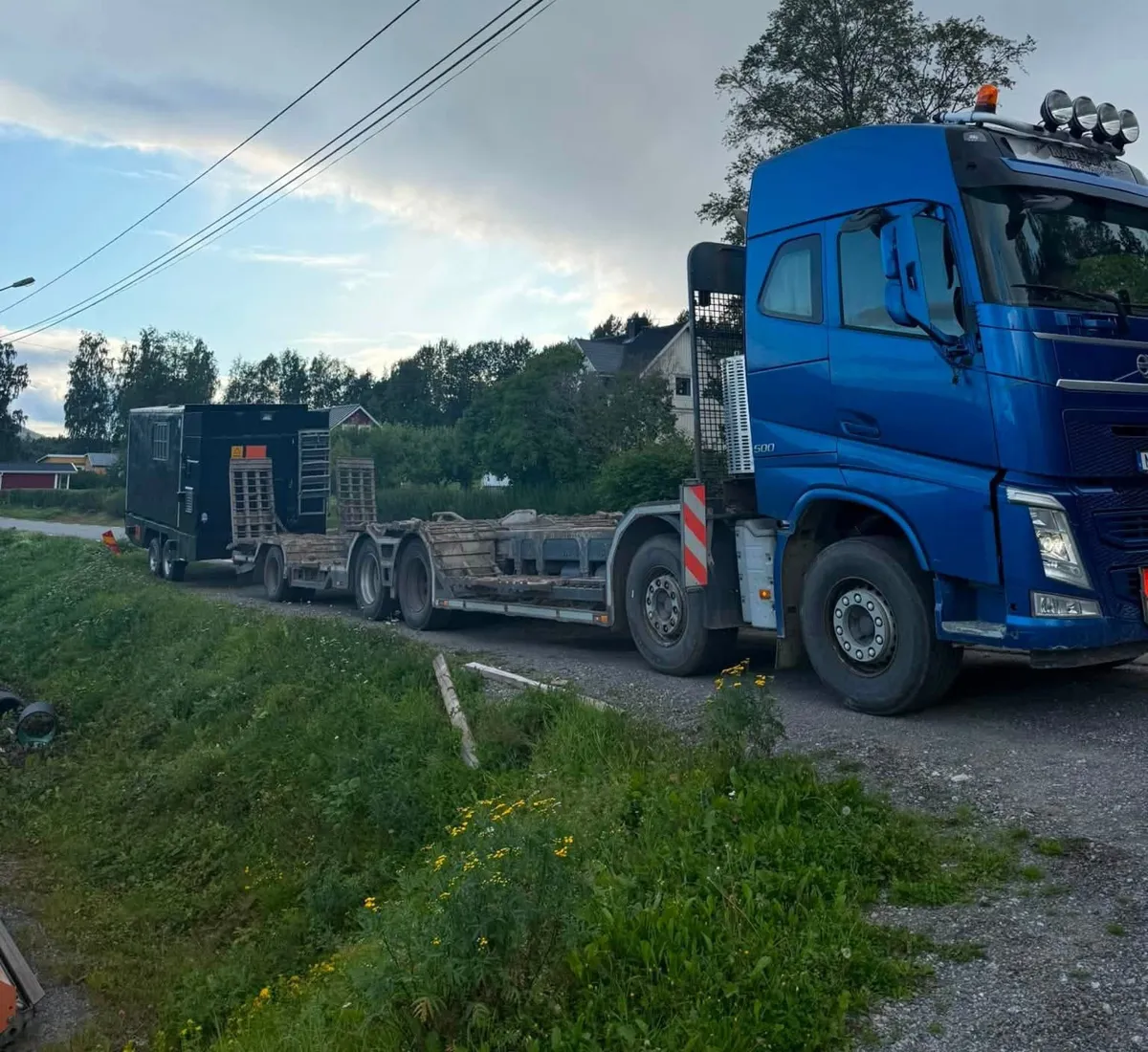 Blå lastbil med maskinsläp och servicevagn på en bygata
