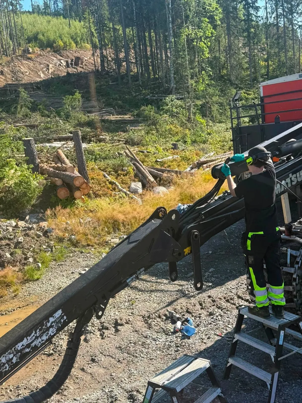 Service på kranen en sommardag, med avverkade stockar i bakgrunden